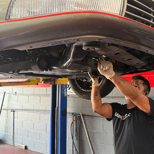 A mechanic completes an oil change under a vehicle in the repair shop