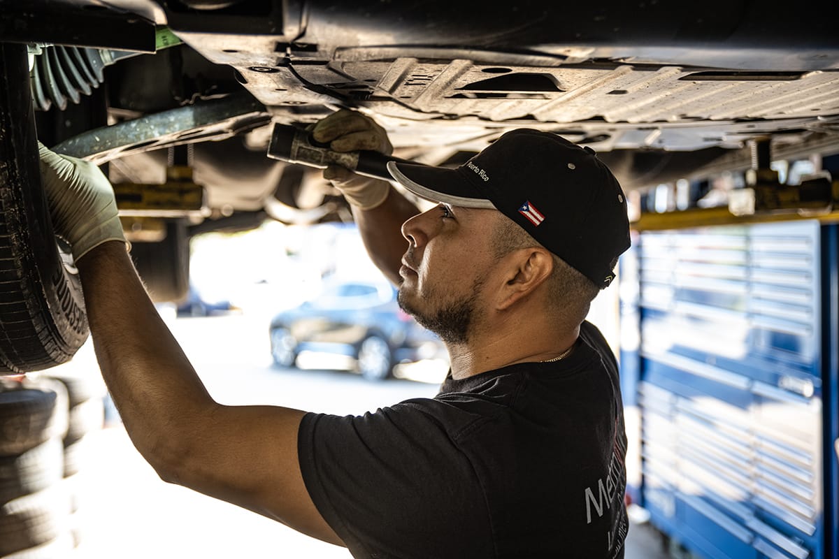 A vehicle technician inspects under a vehicle at a Metro Motor auto repair facility in Arlington, VA