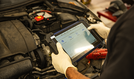 Auto repair mechanic uses advanced diagnostics equipment on a vehicle in an auto repair shop.