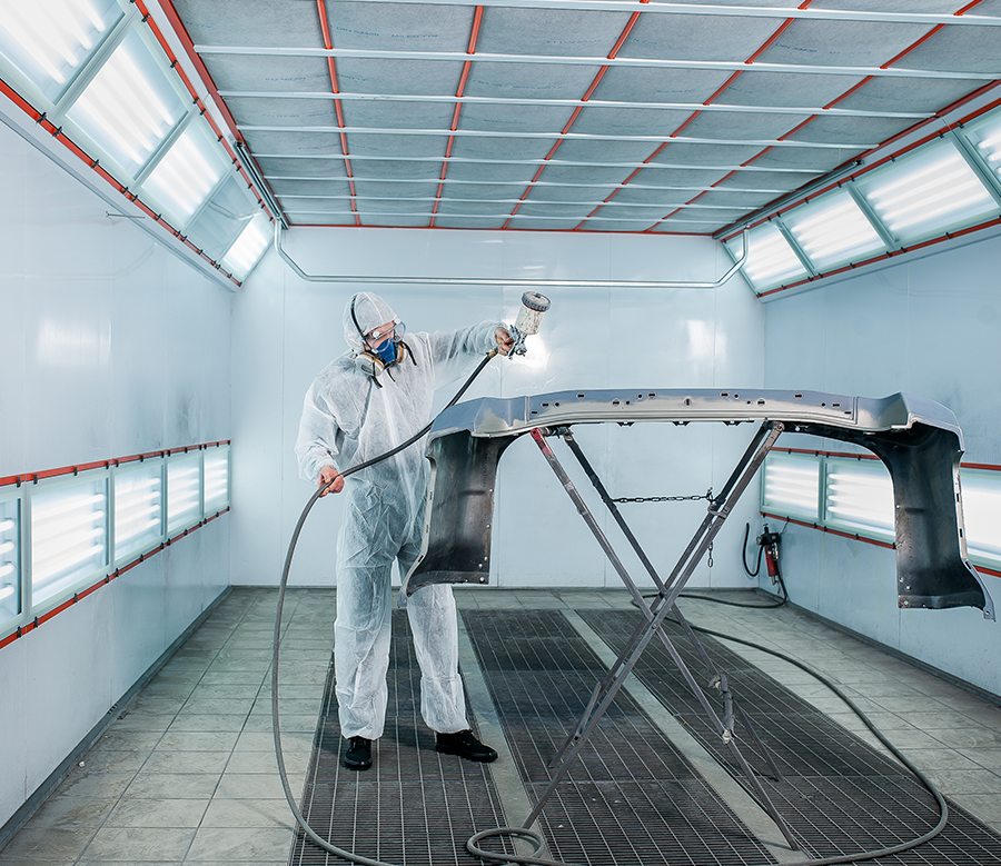 Collision repair specialist paints a vehicle bumper