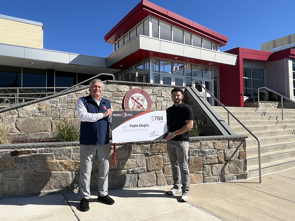 Metro Motor team member presents check to teacher in front of school