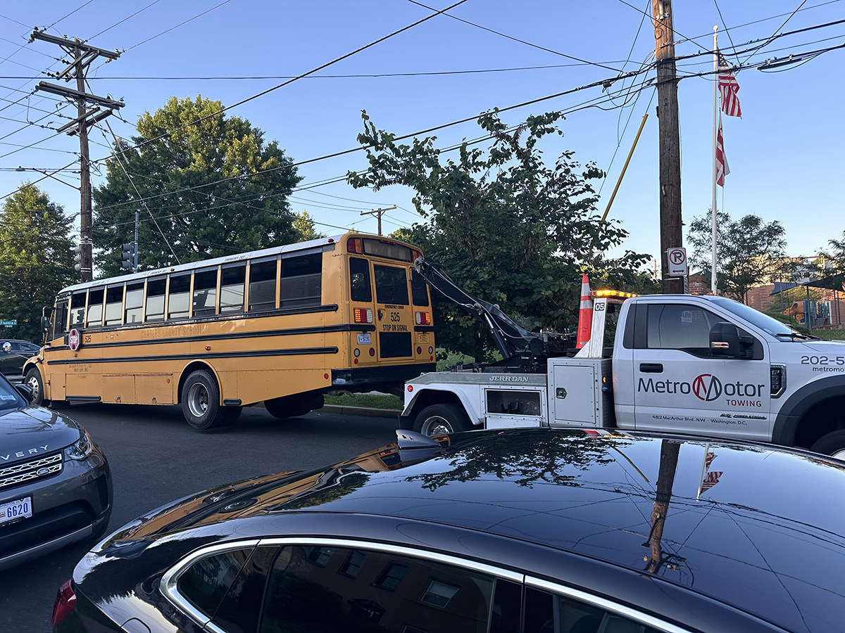A Metro Motor tow truck tows a school bus on a busy street.