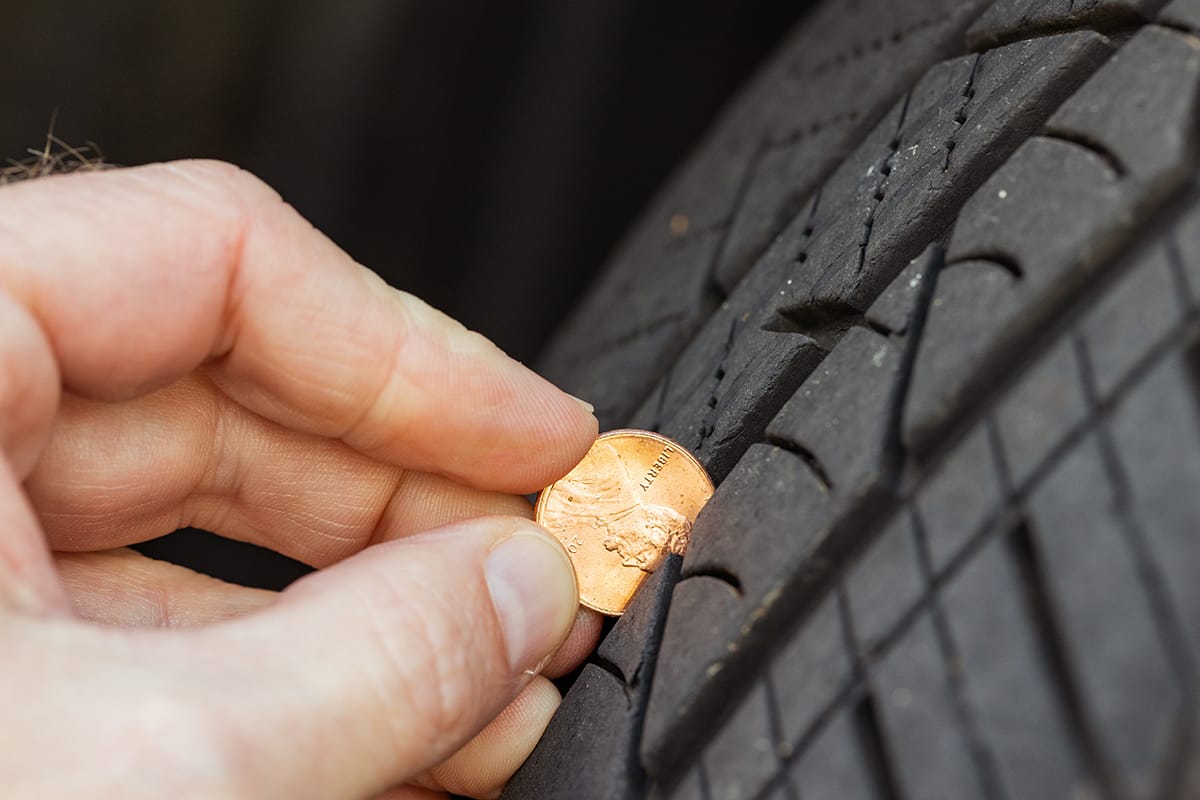 A man inserts a penny into treads to see if the tires need to be replaced.
