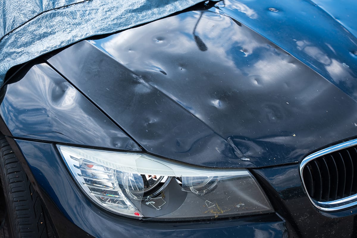 The hood of a BMW shows extensive pock marks from hail damage