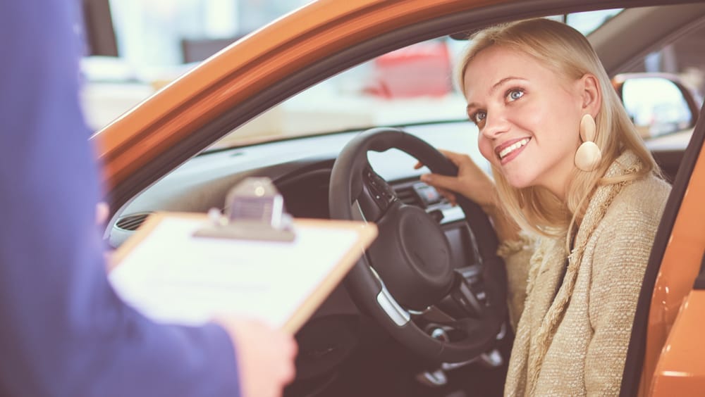 Woman looks up at auto mechanic from the front seat of her car in the auto shop