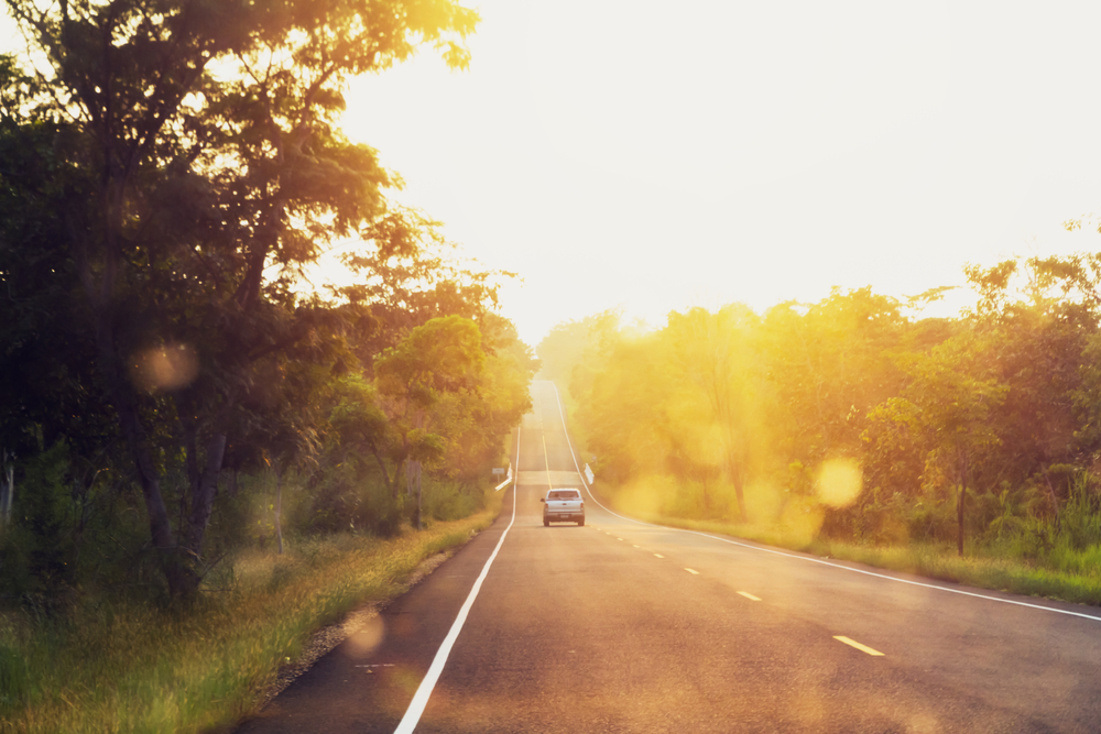 Lone car on a back roads high way, illuminated by a warm sunset