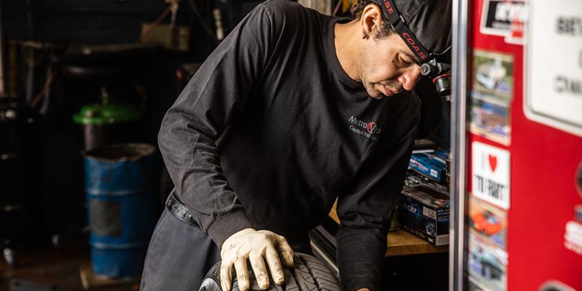 A Metro Motor auto repair technician rolls a tire in the auto repair shop