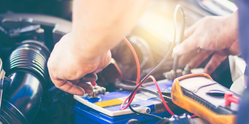 Close up on out-of-frame mechanic working on a car battery 